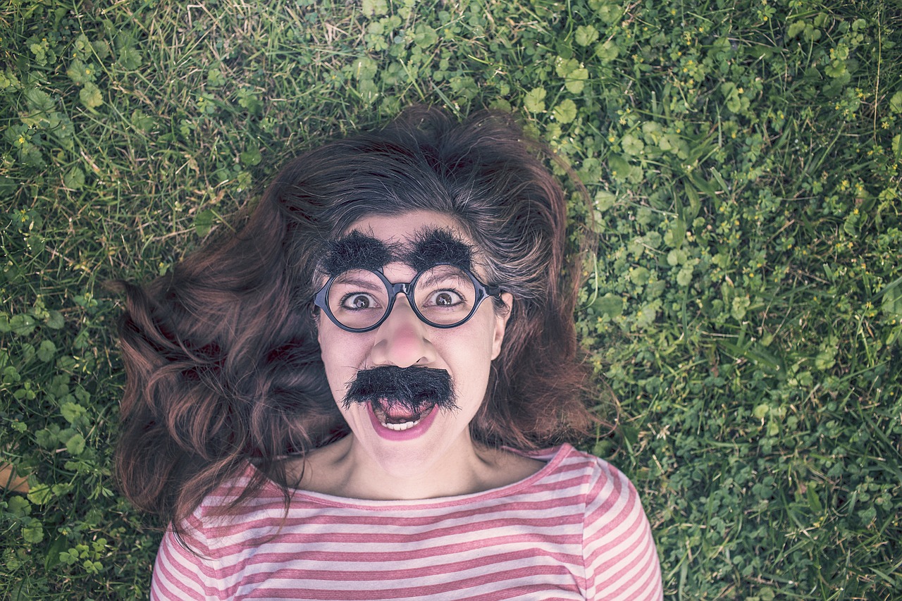 Woman lying on grass wearing comical disguise glasses
